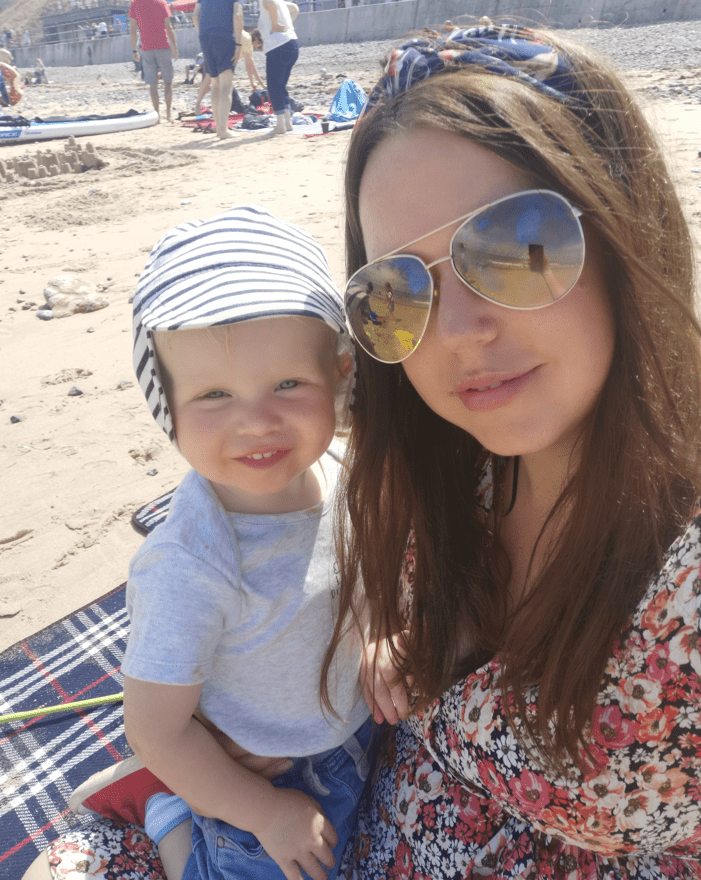 Living kidney donor Sara with her son Joseph, who she donated a kidney to. they are sitting on a blanket at the beach, smiling towards the camera.