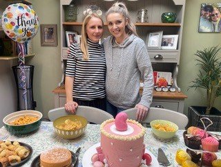 Living kidney donor Ellie alongside her kidney recipient Tess. In front of them is a beautifully decorated pink cake, topped with a marzipan kidney.