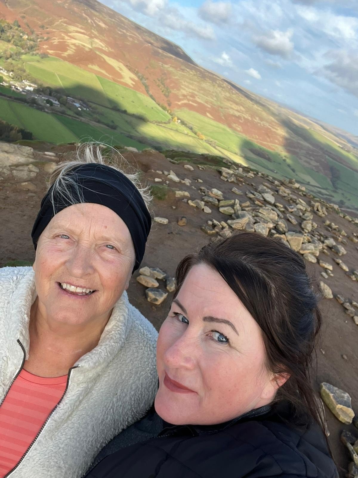 Living kidney recipient Beverley and her donor Lisa taking a selfie at the top of a mountain after a long walk, with the rolling landscape stretching out behind them.