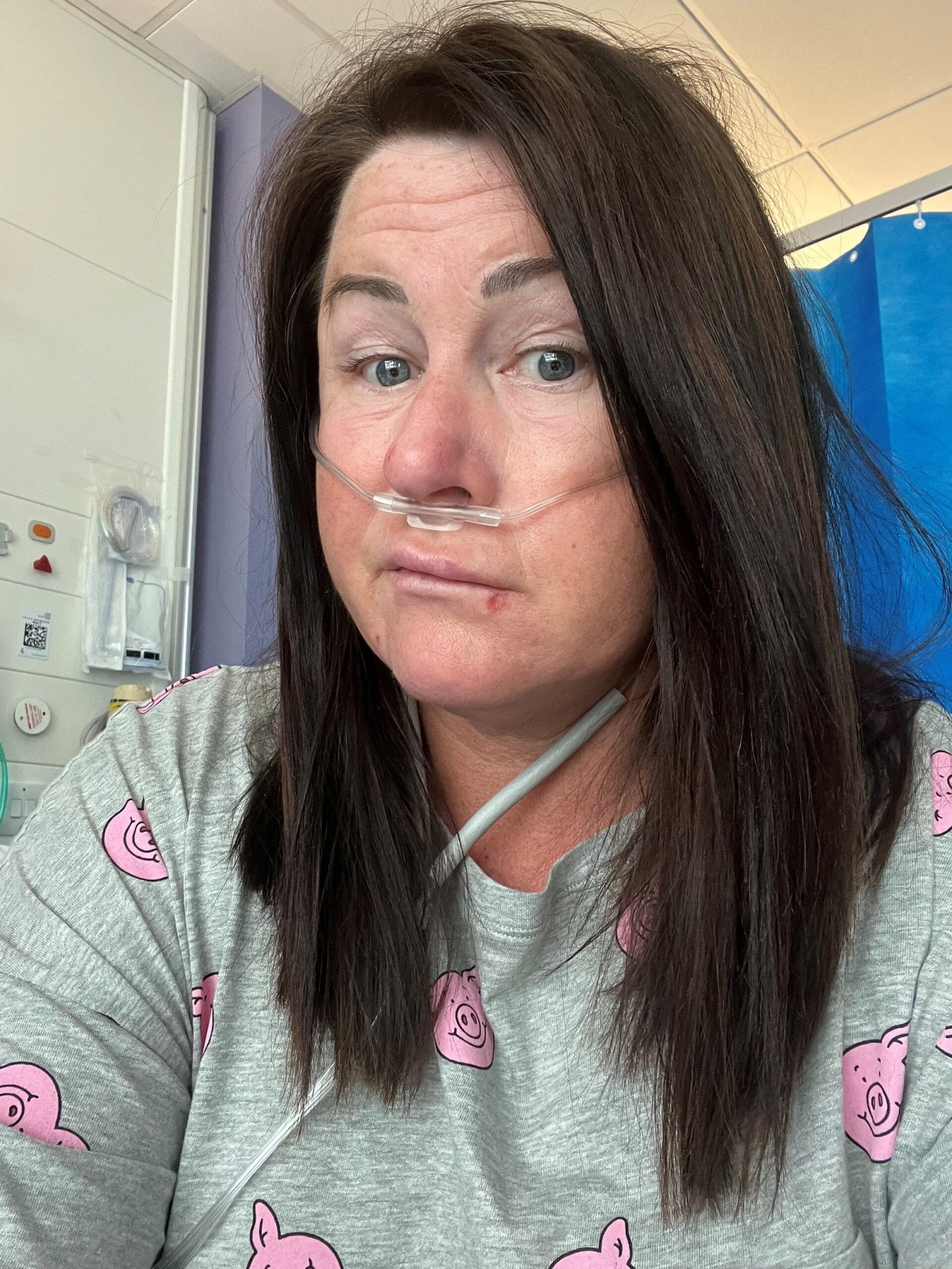 A selfie of living kidney donor Lisa. She is sitting in a hospital weairng a grey top and smirking at the camera.