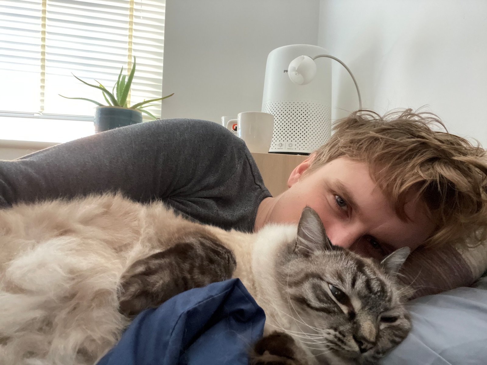 Image of living kidney donor Keegan lying on his bed. In front of his face is one of his cats, cuddling up in front of his face.